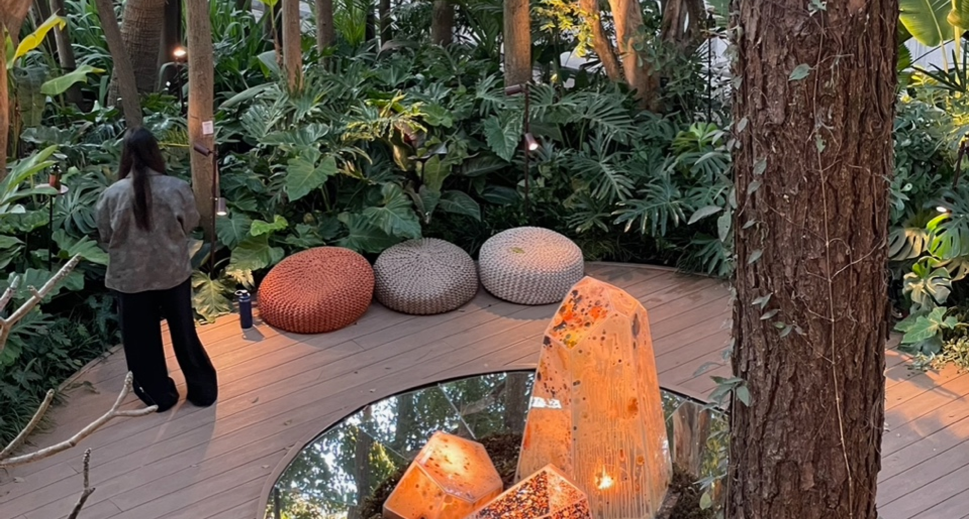 Exposição casa cor 2025. Foto mostra um ambiente externo com grandes pedras de cristais, puffs e vegetação alta ao fundo.