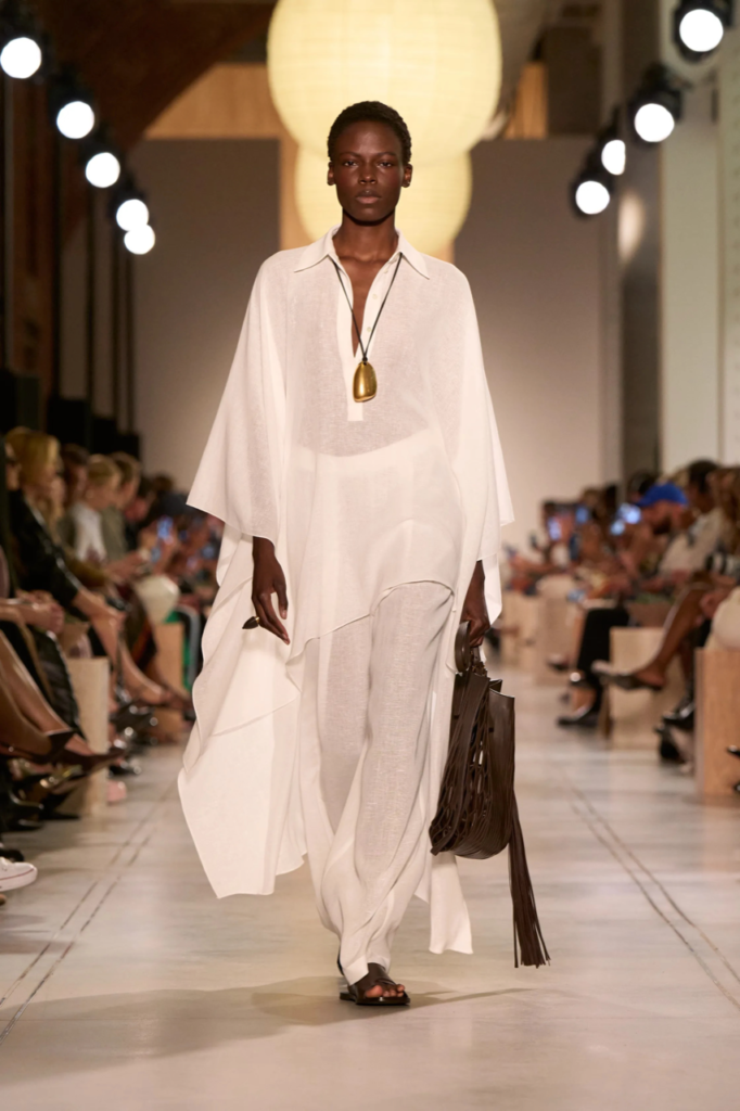 Foto de desfile do estilista Michel Kors na New York Fashion Week 2026. Na foto aparece uma modelo negra usando vestido solto com a cor do ano Pantone: o branco Cloud Dancer.