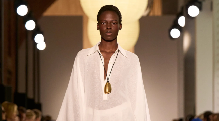 Foto de desfile do estilista Michel Kors na New York Fashion Week 2026. Na foto aparece uma modelo negra usando vestido solto com a cor do ano Pantone: o branco Cloud Dancer.