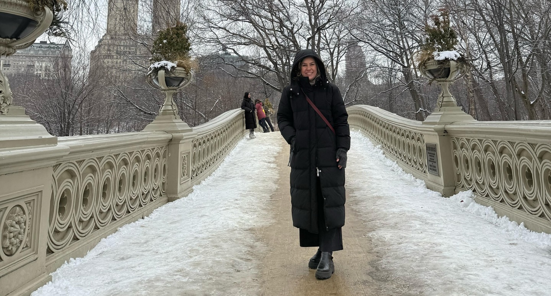 Foto da Silvia Scigliano vestida com botas e sobretudo com capuz em uma ponte com neve em Nova York