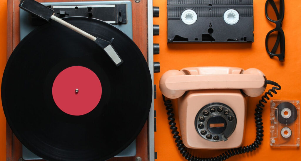 Foto de uma mesa com objetos antigos como telefone de fio, fita cassete e vitrola para demonstrar que as tendências de comportamento para 2026 são mais analógicas e nostáugicas.