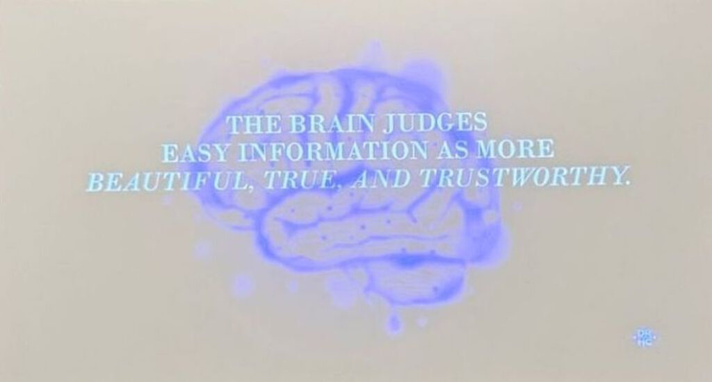 Foto da apresentação sobre moda não ser somente estética na SXSW. Na foto, há um desenho de um cérebro ao fundo. Na frente, há a frase em inglês: O cérebro julga informações fáceis como mais bonitas, verdadeiras e confiáveis.